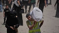  فلسطينيون يحملون أكياس الدقيق التي وزعها برنامج الغذاء العالمي في مدينة غزة، شمال قطاع غزة، السبت 12 يوليو/تموز 2025.