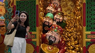 A woman takes a selfie with gods of fortune displayed outside a store selling prosperity items at a shopping mall, in Beijing. 14 July 2025.