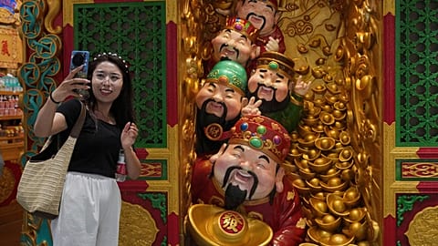A woman takes a selfie with gods of fortune displayed outside a store selling prosperity items at a shopping mall, in Beijing. 14 July 2025.