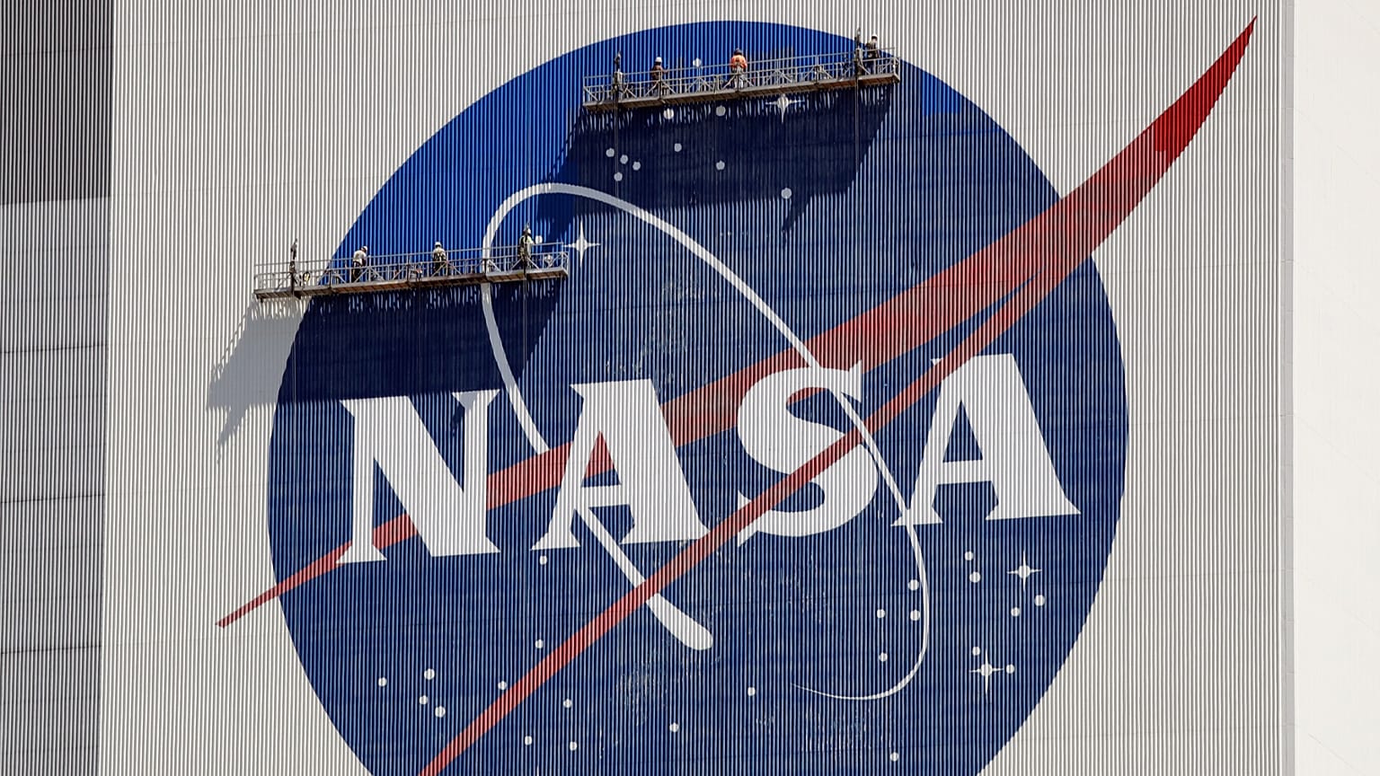 Állványzaton dolgozók festik újra a NASA logóját a floridai Cape Canaveralban található Kennedy Űrközpontban, a Vehicle Assembly Building tetejének közelében.