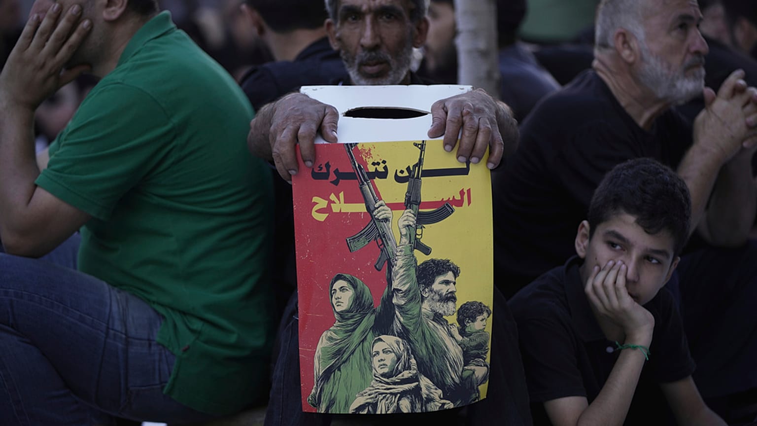  يحمل أحد أنصار حزب الله لافتة كُتب عليها "لن نتخلى عن سلاحنا" بينما يستمع آخرون خلال خطبة لقصة عاشوراء، في الضاحية الجنوبية لبيروت، لبنان، الأحد 6 يوليو/تموز 2025.
