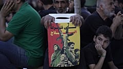  يحمل أحد أنصار حزب الله لافتة كُتب عليها "لن نتخلى عن سلاحنا" بينما يستمع آخرون خلال خطبة لقصة عاشوراء، في الضاحية الجنوبية لبيروت، لبنان، الأحد 6 يوليو/تموز 2025.