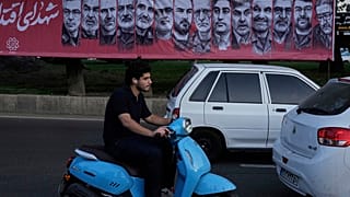 تمر مركبات أمام لافتة تحمل صور قادة القوات المسلحة الإيرانية والعلماء النوويين الذين قُتلوا في الغارات الإسرائيلية