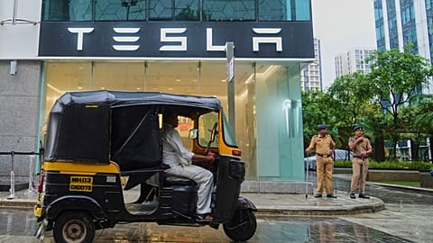 Policemen stand guard as a three-wheeler auto-rickshaw drives past India's first Tesla showroom to be inaugurated in Mumbai, India, Tuesday, July 15, 2025.