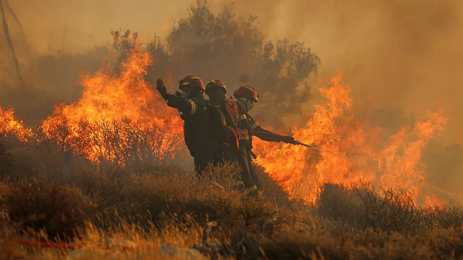 Des pompiers utilisent un tuyau d'arrosage pour tenter d'éteindre le feu près de la ville de Lerapetra, sur la côte sud de l'île de Crète, en Grèce, le 3 juillet. 