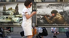 Eine Frau schaut auf ihr Handy, während sie an einer Straßenausstellung mit kolorierten Fotos aus der Zeit des Zweiten Weltkriegs in St. Petersburg, Russland, vorbeigeht, am Montag, 14. Juli 2025