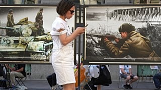 Una donna guarda il suo telefono mentre passa davanti a una mostra di foto colorate dell'epoca della Seconda Guerra Mondiale a San Pietroburgo, in Russia, lunedì 14 luglio 2025.