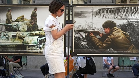 A woman looks at her phone while passing a street exhibition of World War II-era colorized photos in St. Petersburg, Russia, on Monday, July 14, 2025