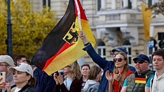 أشخاص يحملون العلم الألماني في حفل تنصيب رسمي للواء ألماني على الجناح الشرقي لحلف شمال الأطلسي