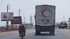 مقاتلون يركبون دراجة نارية أمام قافلة من المركبات محملة بالمواد الغذائية والمساعدات الأخرى في طريقهم إلى السويداء على الطريق السريع الدولي في ريف درعا ، سوريا ، الأحد 20 يوليو