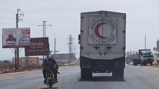 مقاتلون يركبون دراجة نارية أمام قافلة من المركبات محملة بالمواد الغذائية والمساعدات الأخرى في طريقهم إلى السويداء على الطريق السريع الدولي في ريف درعا ، سوريا ، الأحد 20 يوليو