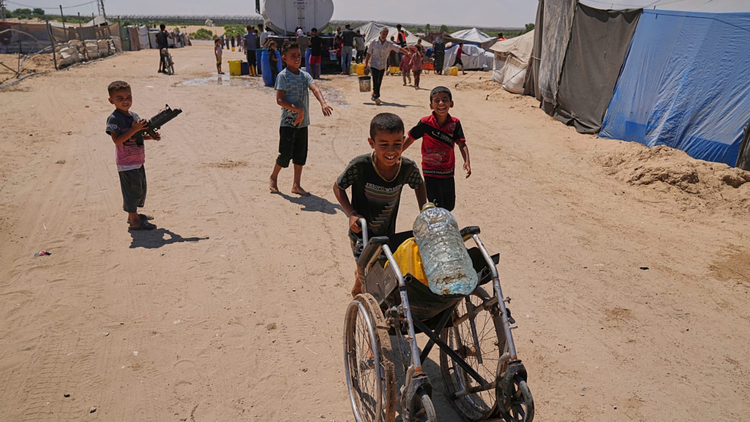 طفل فلسطيني يدفع كرسيًا متحركًا بداخله عبوة مياه وزجاجة بلاستيكية، جنوب قطاع غزة، السبت 19 يوليو 2025.