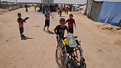 طفل فلسطيني يدفع كرسيًا متحركًا بداخله عبوة مياه وزجاجة بلاستيكية، جنوب قطاع غزة، السبت 19 يوليو 2025.