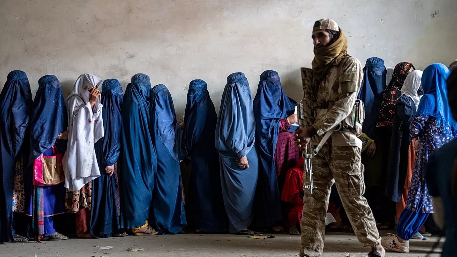 A Taliban fighter stands guard as women wait to receive food rations distributed by a humanitarian aid group in Kabul, 23 May, 2023