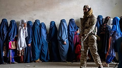 Un combattente talebano sta di guardia mentre le donne aspettano di ricevere le razioni di cibo distribuite da un gruppo di aiuti umanitari a Kabul, 23 maggio 2023