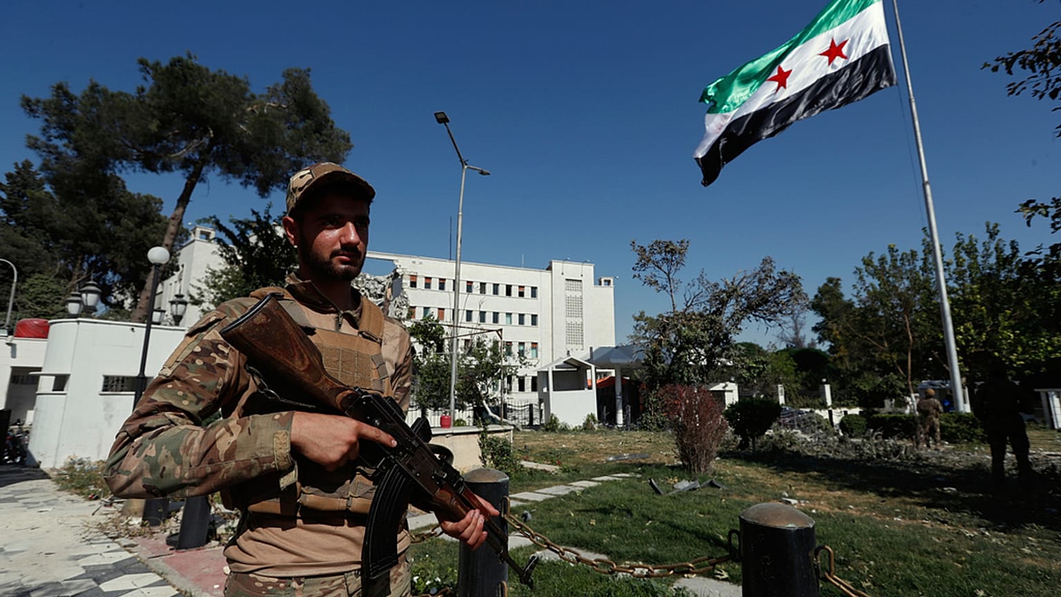 Syrian soldiers raise the Syrian national flag in front of the Syrian Defense Ministry building, which was heavily damaged by Israeli airstrikes last Wednesday, in Damascus, S