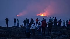 Eine Gruppe von Besuchern versammelt sich auf einem Hügel, nur wenige Kilometer entfernt, um die beiden aktiven Krater nach einem Vulkanausbruch etwa sechs Kilometer nördlich von Grindavík in Island am 19.07.2025 zu beobachten.