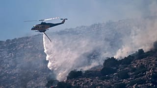 Un hélicoptère de pompiers largue de l'eau lors de la lutte contre un incendie dans la zone balnéaire de Charakas, le 26 juin 2025
