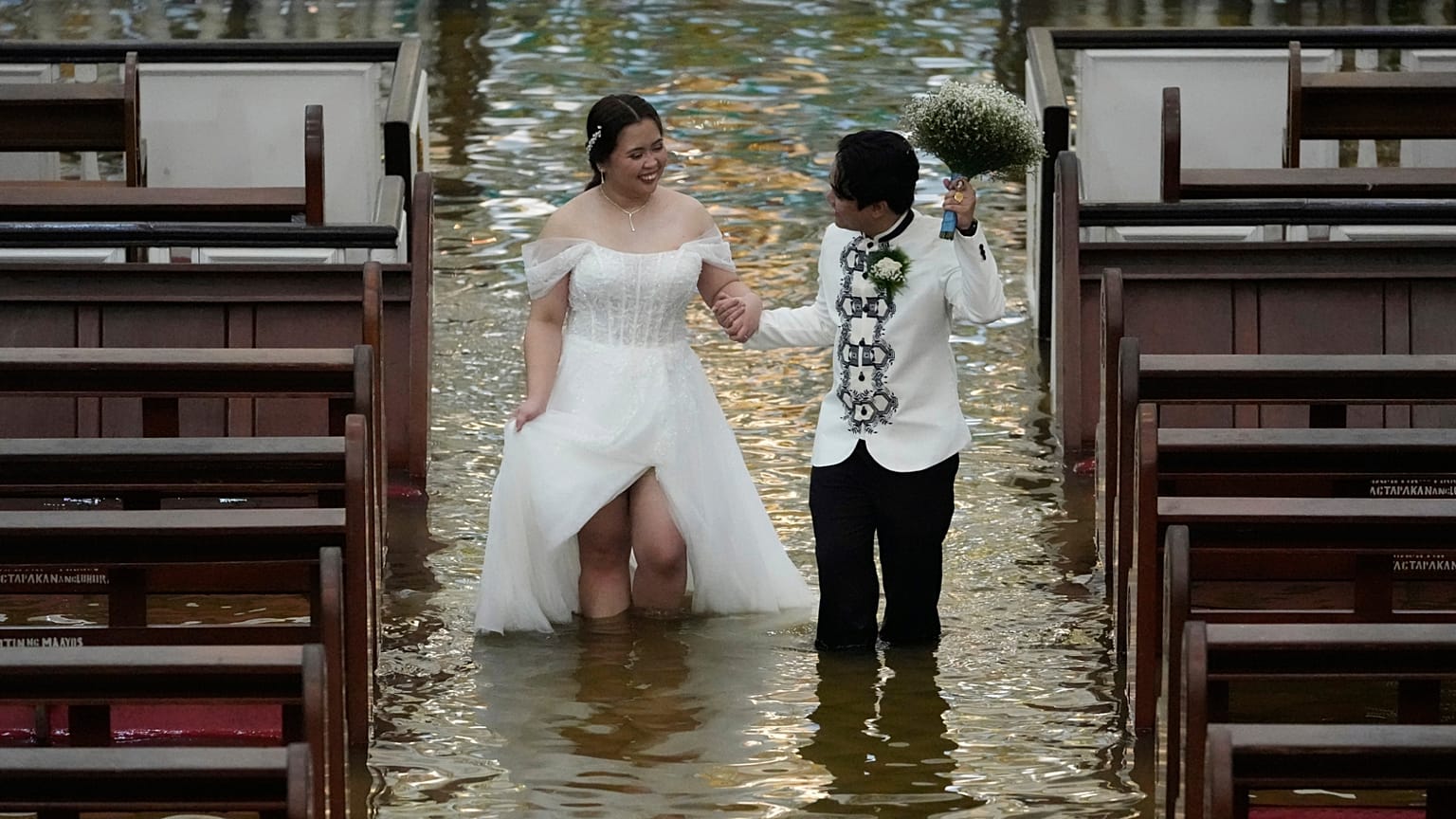 Les jeunes mariés Jade Rick Verdillo et Jamaica marchent main dans la main lors de leur mariage à l'église inondée de Barasoain à Malolos, dans la province de Bulacan, aux Philippines, le 22.07.2025