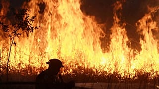 Um agente da polícia pulveriza água numa tentativa de extinguir um incêndio que lavra num campo de turfa em Ogan Ilir, 20 de julho de 2025