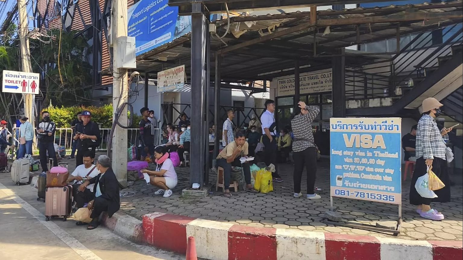 Des personnes sont assises près d'un poste de contrôle frontalier entre la Thaïlande et le Cambodge dans la province de Sa Kaeo, le 24 juin 2025