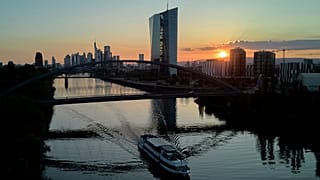 O sol põe-se atrás do Banco Central Europeu, à direita, e dos edifícios da zona bancária em Frankfurt, Alemanha, terça-feira, 1 de julho de 2025