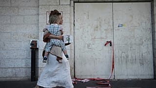 امرأة تحمل طفلها عبر شريط مسرح الجريمة في موقع هجوم أسفر عن مقتل رجل إسرائيلي في مركز تسوق في تقاطع غوش عتصيون بالضفة الغربية ، الخميس 10 يوليو / تموز 2025.