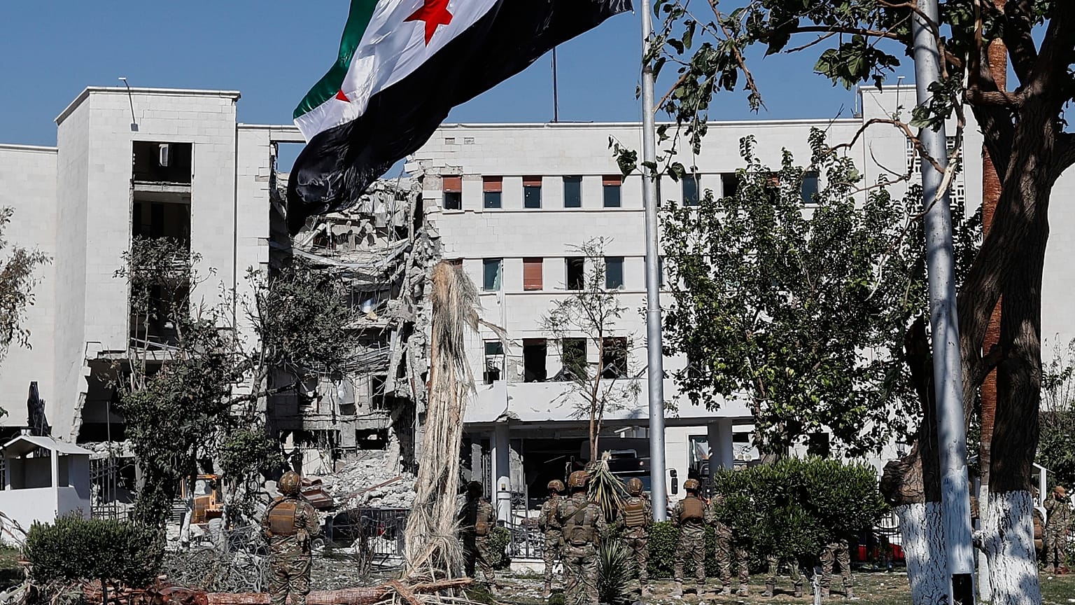 جنود يرفعون العلم السوري أمام مبنى وزارة الدفاع في دمشق، سوريا، السبت 19 يوليو/ تموز 2025، والذي تعرض لأضرار جسيمة جراء الغارات الجوية الإسرائيلية.