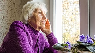 Una mujer mayor mira por la ventana.