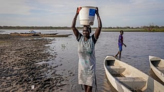 Eine Frau trägt Wasser auf dem Kopf aus einem Sumpf, da ein Großteil des Gebiets aufgrund jahrelanger Überschwemmungen keinen Zugang zu sauberem Trinkwasser hat, in Canal-Pigi County, So