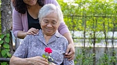 Un cuidador y una anciana observan una flor.