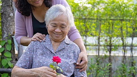 A caregiver and an elderly woman look at a flower.