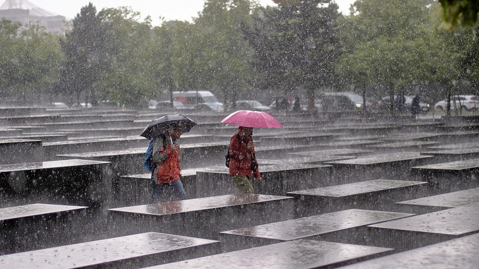 Dois visitantes caminham pelo Memorial do Holocausto sob chuva forte em Berlim, Alemanha, quinta-feira, 5 de junho de 2025
