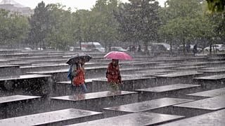 Dois visitantes caminham pelo Memorial do Holocausto sob chuva forte em Berlim, Alemanha, quinta-feira, 5 de junho de 2025
