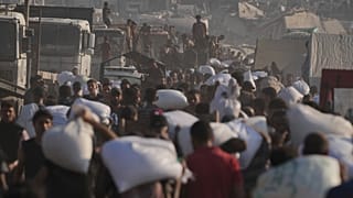 Palestinianos carregam sacos de farinha descarregados de um comboio de ajuda humanitária que chegou à Cidade de Gaza vindo do norte da Faixa de Gaza, 26 de julho de 2025