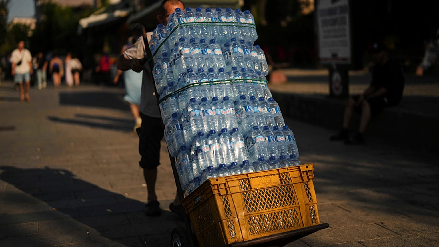 Um homem entrega garrafas de plástico de água num restaurante popular num dia quente de verão em Istambul, Turquia, quinta-feira, 24 de julho de 2025