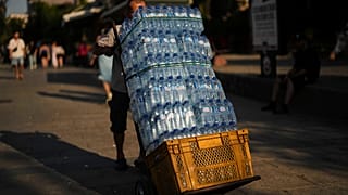 Um homem entrega garrafas de plástico de água num restaurante popular num dia quente de verão em Istambul, Turquia, quinta-feira, 24 de julho de 2025