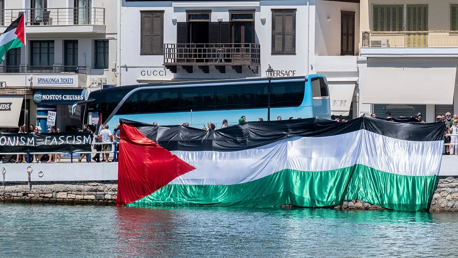 Manifestantes propalestinos se reúnen durante la llegada de un barco que transporta turistas israelíes, al fondo, en el puerto de Agios Nikolaos, en la isla de Creta, Grecia.