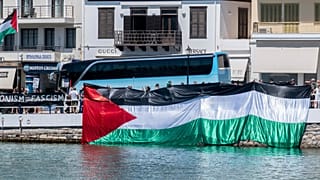 Manifestantes propalestinos se reúnen durante la llegada de un barco que transporta turistas israelíes, al fondo, en el puerto de Agios Nikolaos, en la isla de Creta, Grecia.