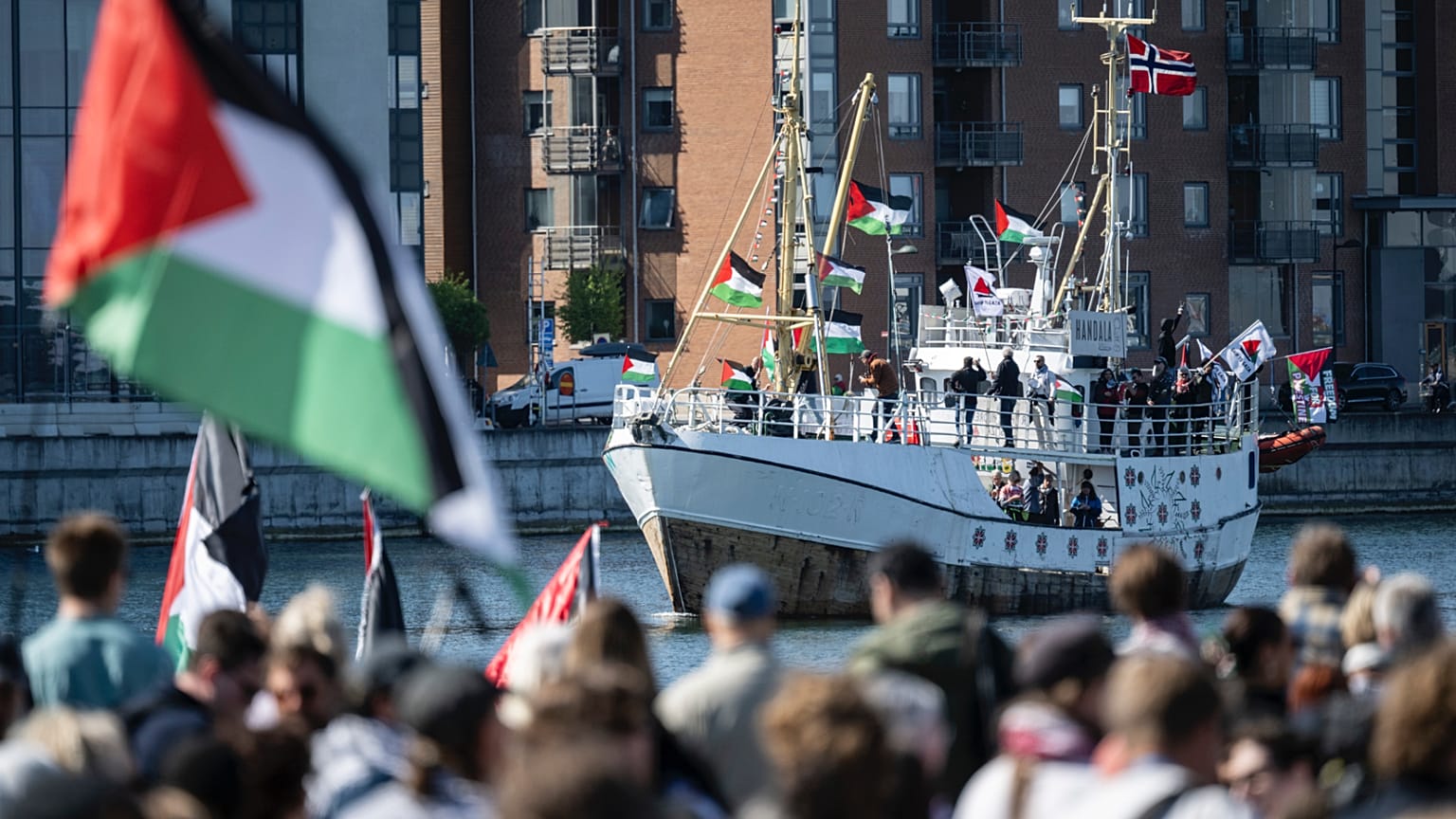 متظاهرون يحملون أعلامًا فلسطينية يراقبون سفينة "حنظلة" المتجهة إلى غزة وهي تصل إلى ميناء مالمو بالسويد، الأربعاء 8 مايو/ أيار 2024.