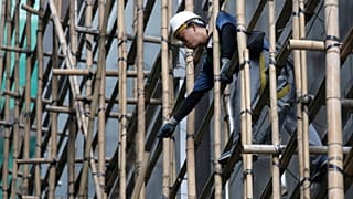A worker builds a bamboo scaffolding around a building. 27.08.2015