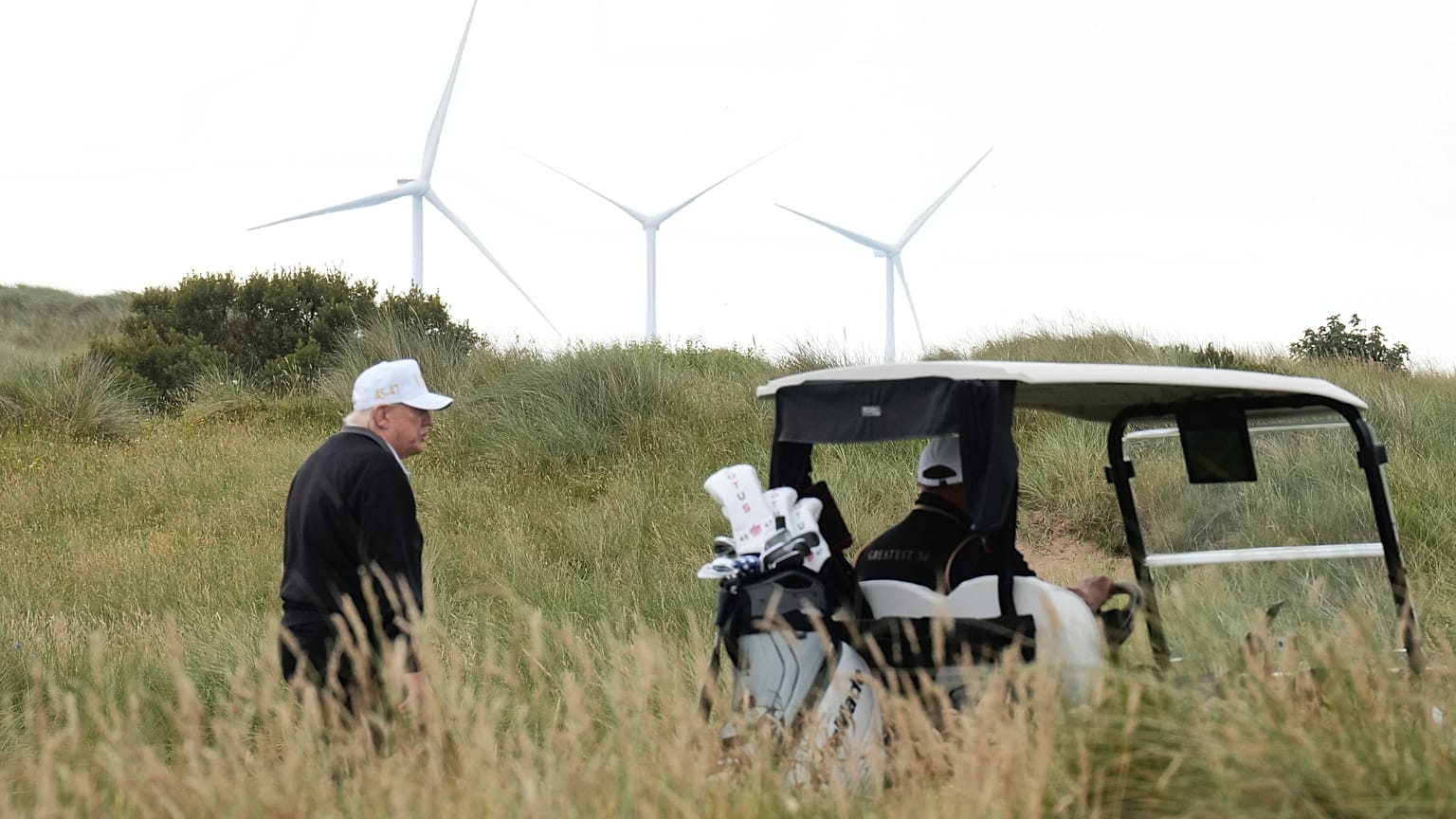 Le président Donald Trump marche au milieu d'éoliennes lors de la cérémonie d'ouverture du terrain de golf Trump International Golf Links, près d'Aberdeen, en Écosse.