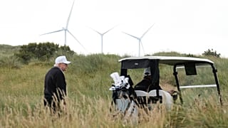 Präsident Donald Trump spaziert während der Eröffnungsfeier des Trump International Golf Links Golfplatzes in der Nähe von Aberdeen, Schottland, vor dem Hintergrund von Windturbinen.