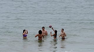 Veraneantes brincam com uma bola na água na praia de Carcavelos, nos arredores de Lisboa