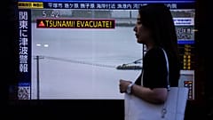Bir yaya, 30 Temmuz 2025 Çarşamba günü Tokyo'da tsunami uyarısı gösteren bir TV ekranının önünden geçiyor.
