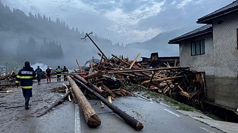 First responders walk by damages after a flash flood in the village of Brosteni, northern Romania, Monday, July 28, 2025.