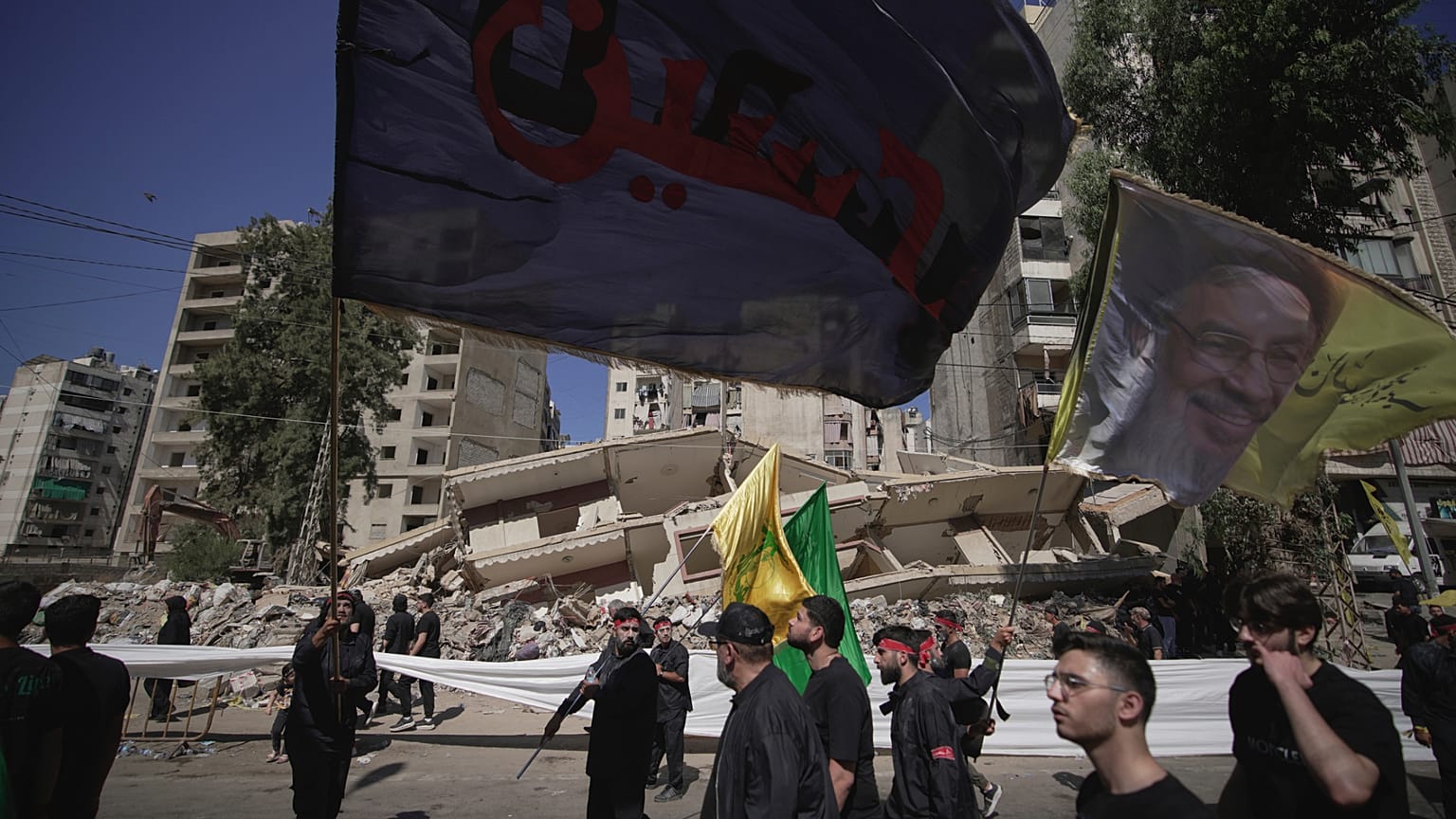 أنصار حزب الله يسيرون أمام مبنى دمرته غارة جوية إسرائيلية في الضاحية الجنوبية لبيروت، لبنان، الأحد 6 يوليو/تموز 2025.