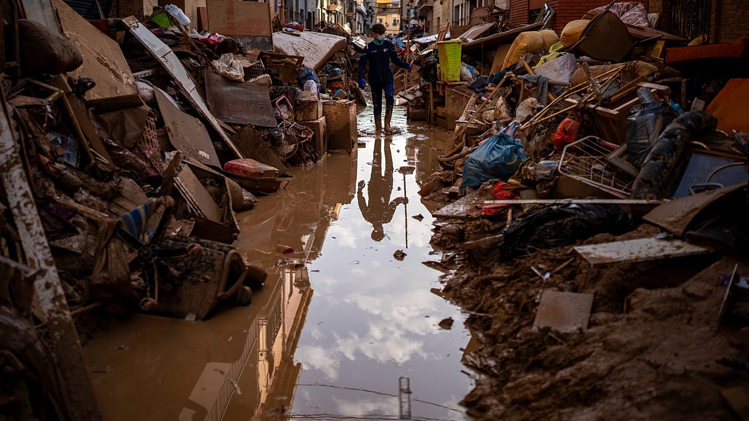 Una persona camina por una calle con muebles amontonados y basura a los lados en una zona afectada por las inundaciones en Paiporta, Valencia, España
