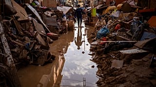 Una persona camina por una calle con muebles amontonados y basura a los lados en una zona afectada por las inundaciones en Paiporta, Valencia, España