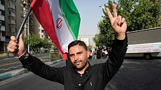 رجل يرفع علامة النصر ويحمل العلم الإيراني أثناء حضوره مراسم جنازة جنرالات القوات المسلحة الإيرانية في شارع آزادي، في طهران، إيران، السبت 28 يونيو 2025.
